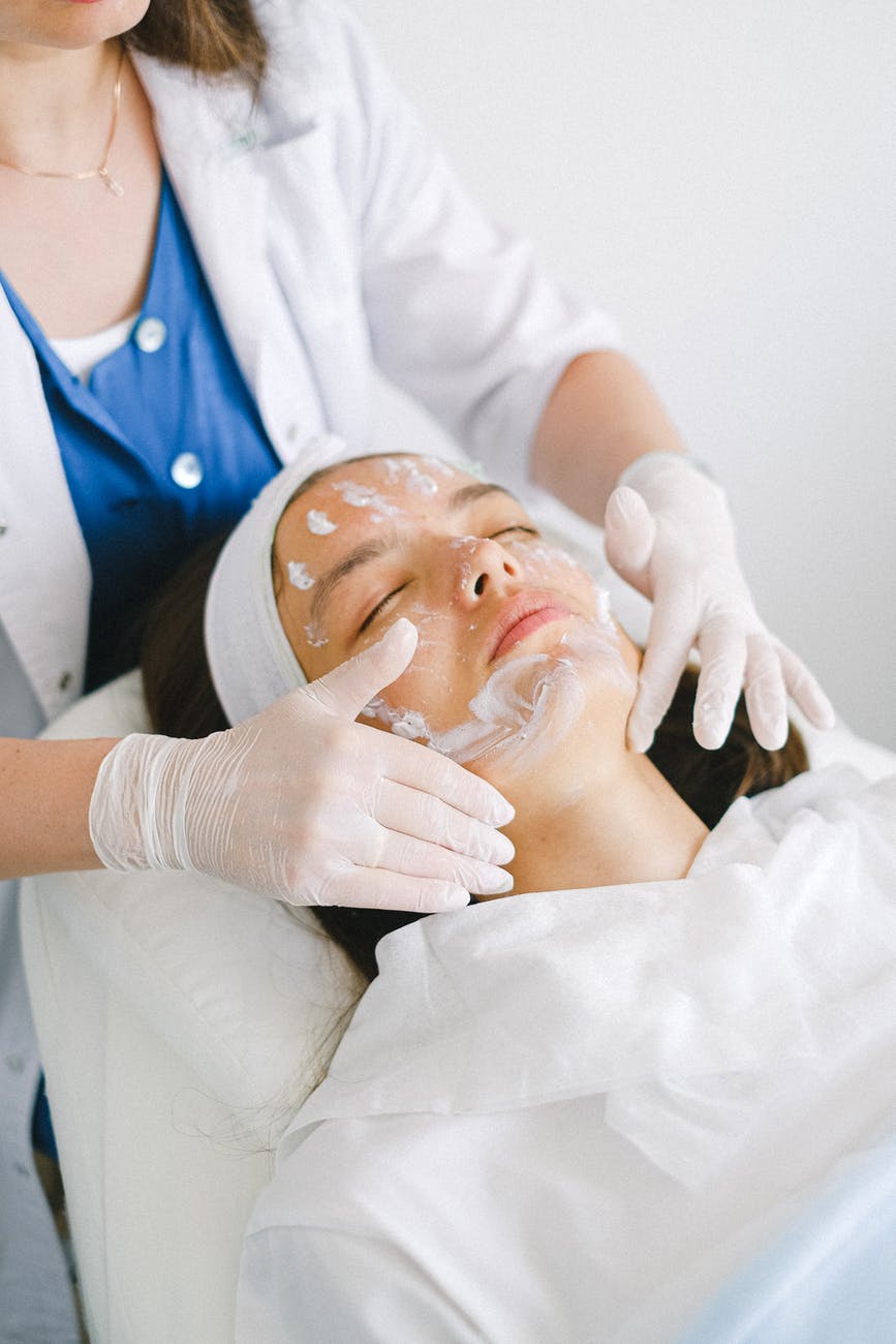 cosmetologist applying facial mask on customer face in spa salon